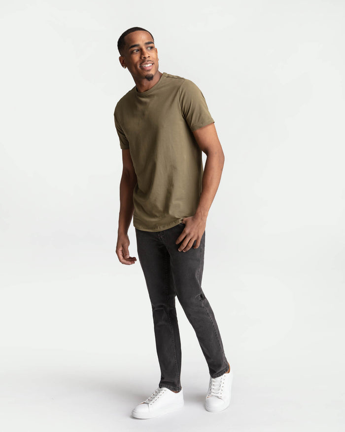 Man wearing olive short-sleeve t-shirt and faded black skinny fit jeans with white sneakers.