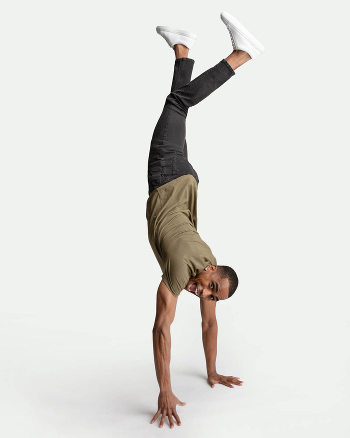 Man wearing faded black skinny fit jeans and tan shorts, performing a handstand.