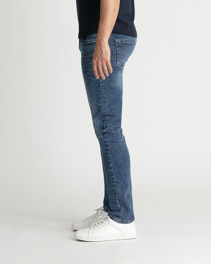 Man wearing medium blue skinny fit jeans with white sneakers, shown from side view.