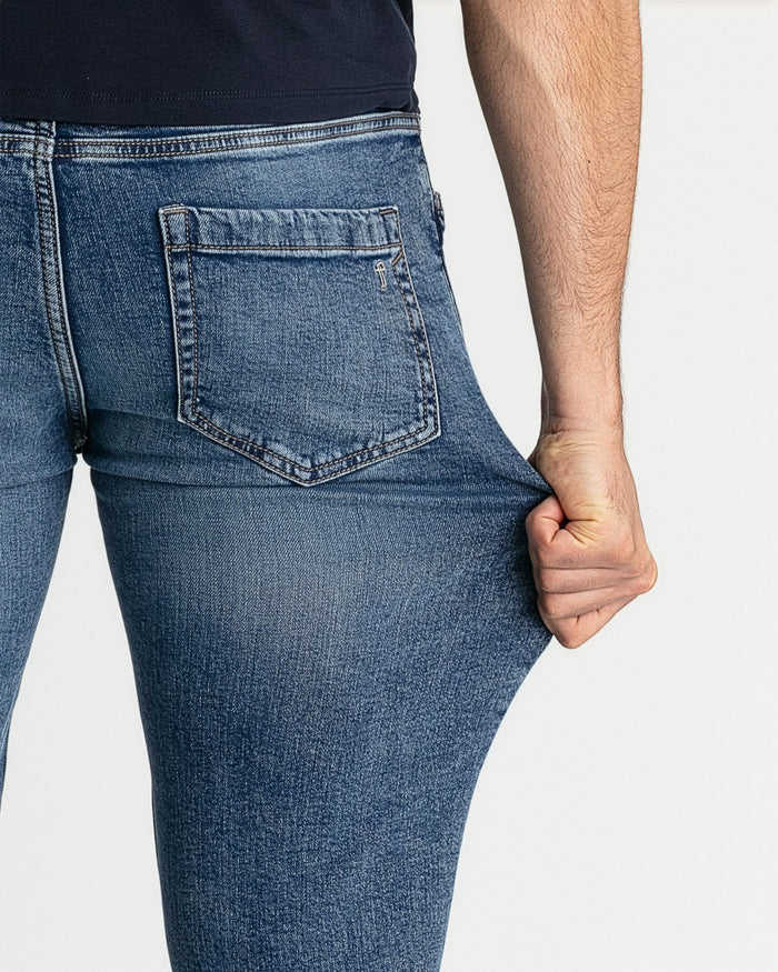Medium blue skinny fit jeans with back pocket detail shown on model wearing navy shirt.