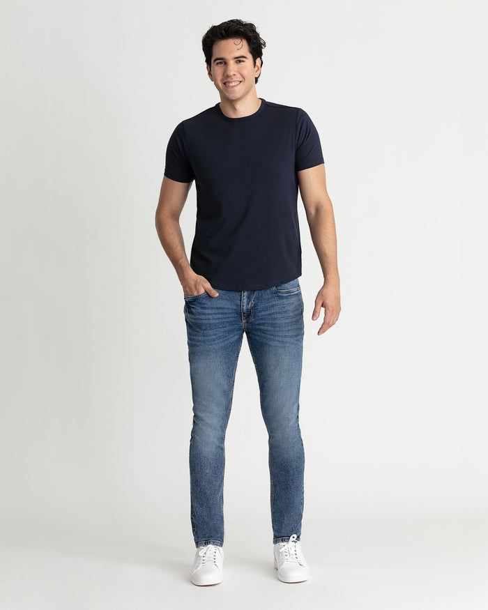 Man wearing navy short-sleeve t-shirt and medium blue skinny fit jeans with white sneakers.