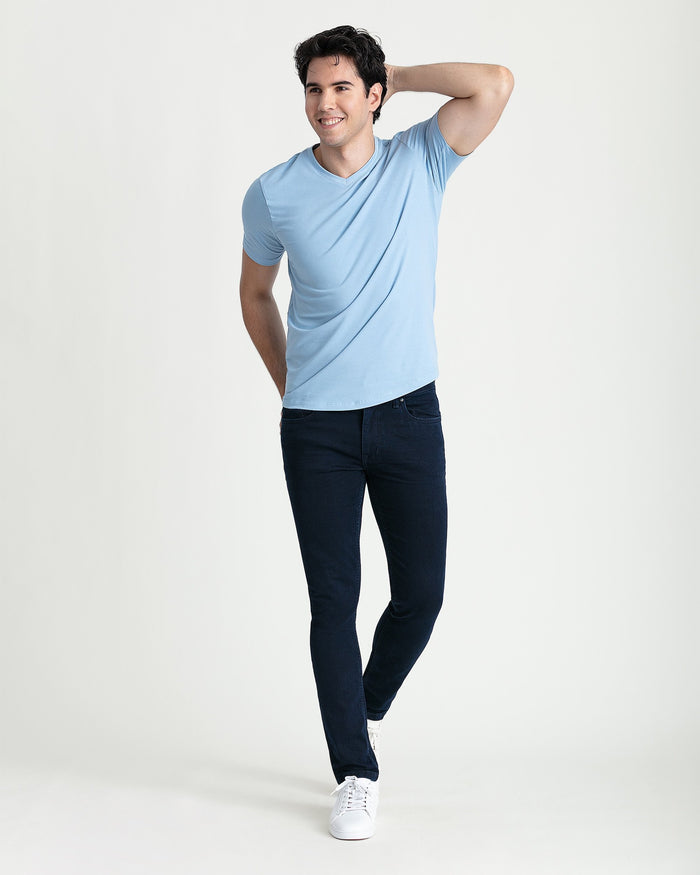 Man wearing light blue v-neck t-shirt and dark navy skinny fit jeans with white sneakers.