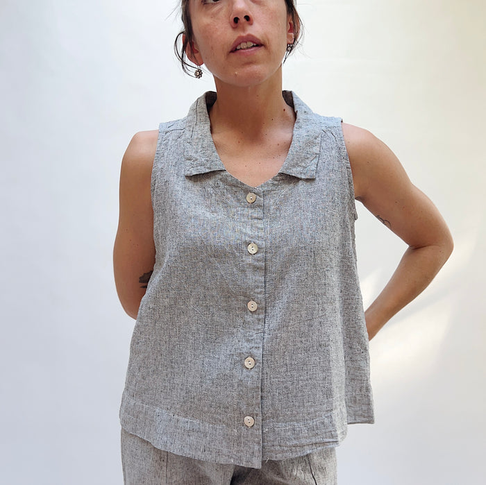 Person wearing a sleeveless gray button-up shirt against a plain background