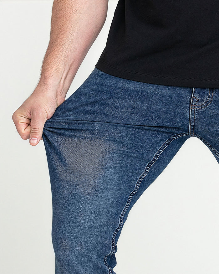 Man wearing medium blue slim fit jeans with black shirt, showing fit at thigh and waistband.