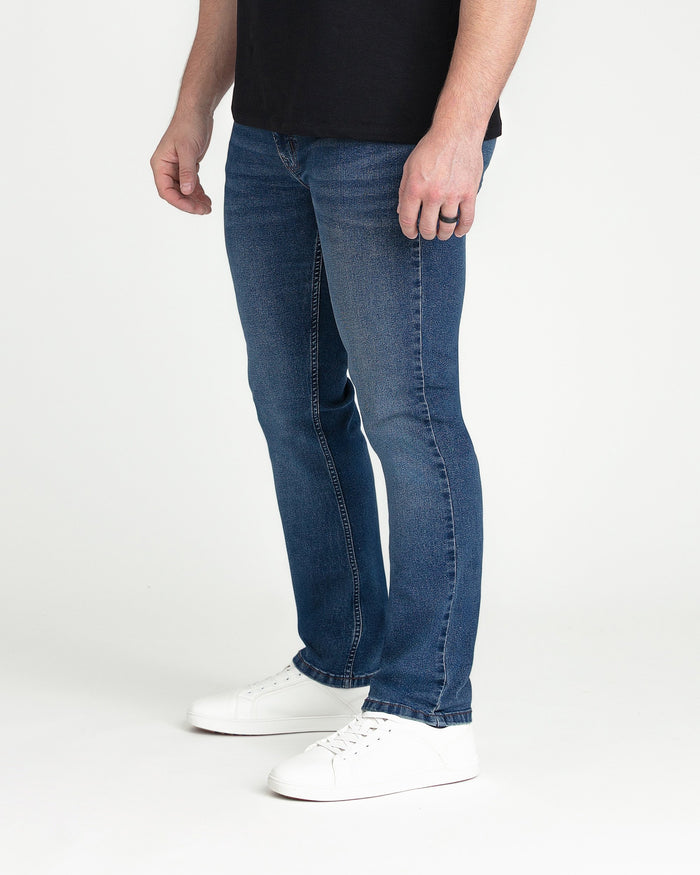 Man wearing medium blue slim fit jeans with black t-shirt and white sneakers.