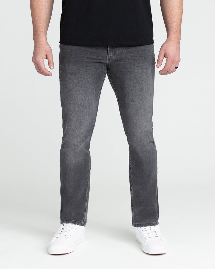 Grey slim fit jeans with straight leg on a model wearing black shirt and white sneakers.
