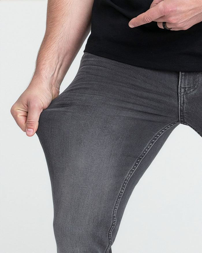 Man wearing black T-shirt and grey slim fit denim jeans with visible stitching detail.