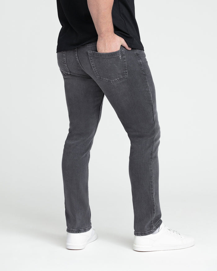 Grey slim fit jeans with back pocket detail, shown on model wearing white sneakers.