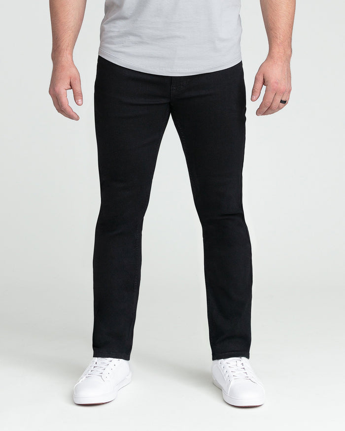 Man wearing black slim fit jeans with white sneakers and light gray t-shirt.