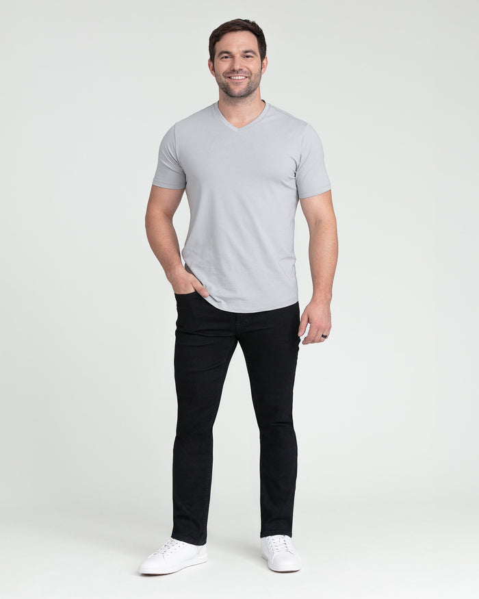 Man wearing light gray v-neck t-shirt and black slim fit jeans with white sneakers.
