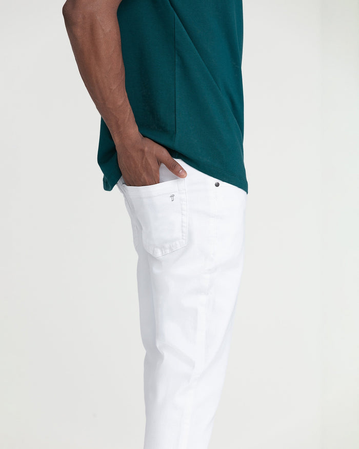 White slim fit jeans with button closure and back pocket detail on model wearing teal shirt.