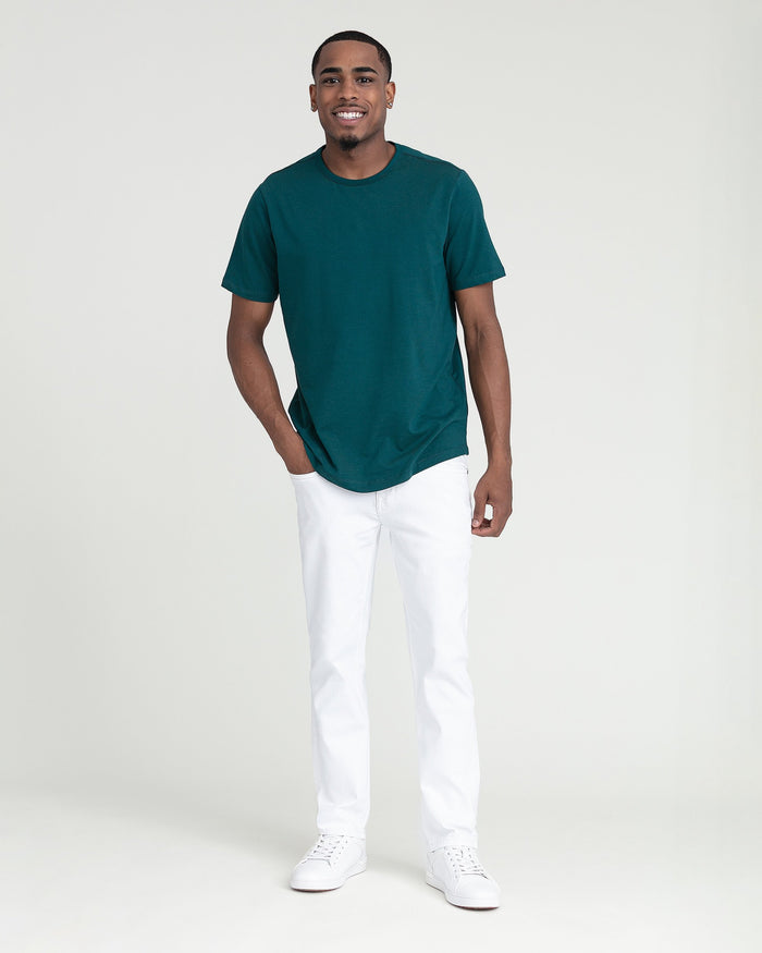 Man wearing teal crew neck t-shirt and white slim fit pants with white sneakers.