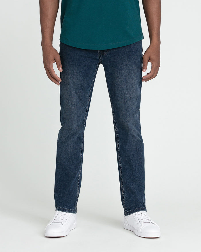 Man wearing teal crew neck shirt and dark blue slim fit jeans with white sneakers.
