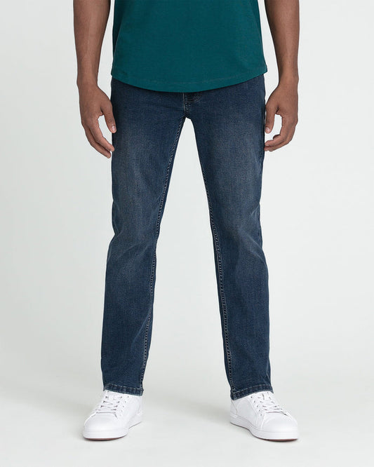 Man wearing teal crew neck shirt and dark blue slim fit jeans with white sneakers.