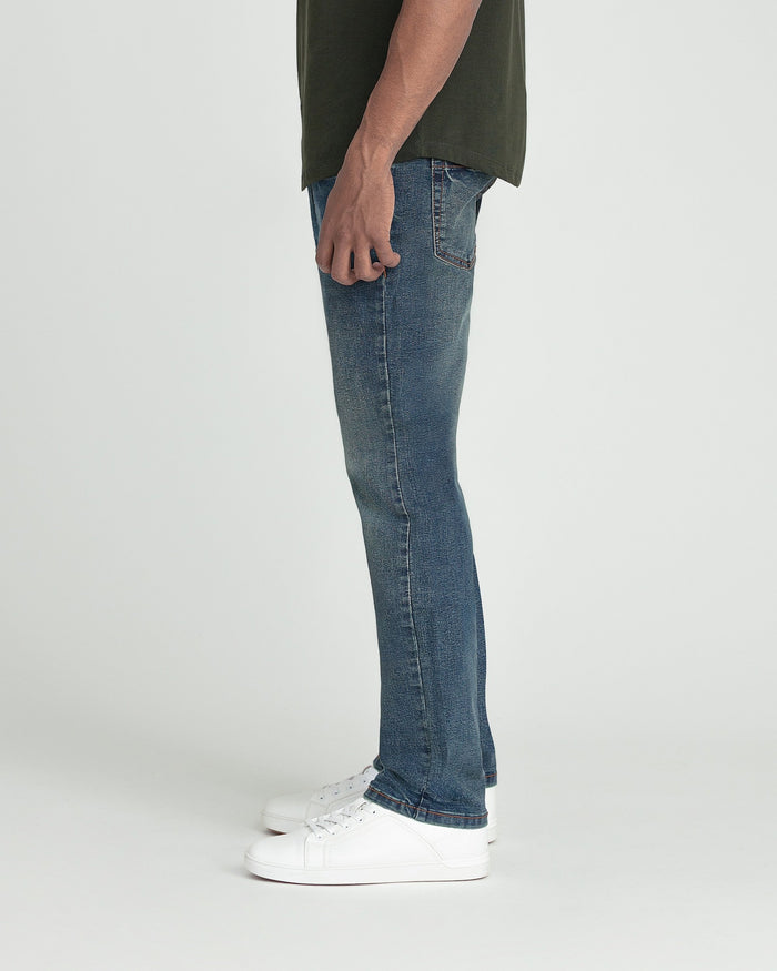 Slim fit blue jeans with tinted wash and slight flare at hem, paired with white sneakers.