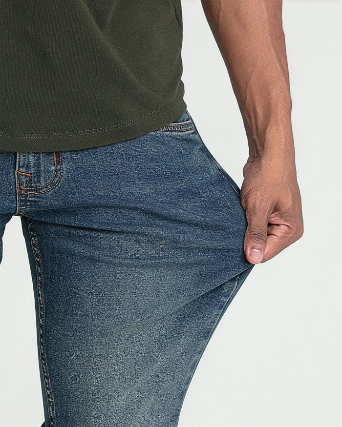 Man wearing olive green t-shirt and medium wash slim fit jeans with orange stitching detail at waistband.