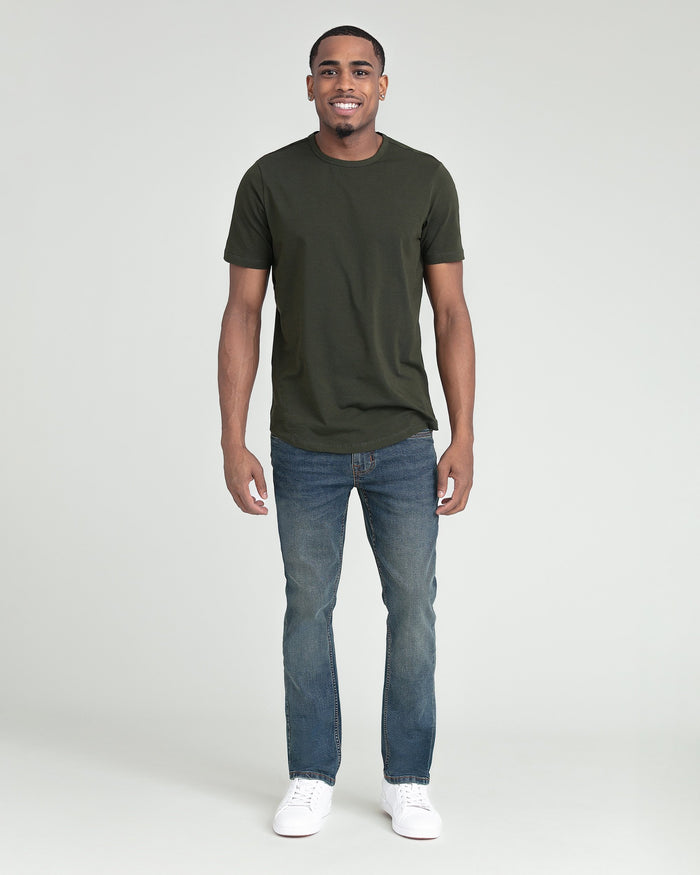 Man wearing olive green t-shirt and blue slim fit jeans with white sneakers.