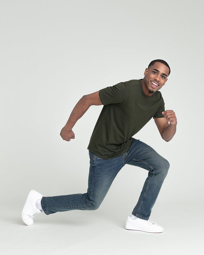 Man wearing olive green short-sleeve t-shirt with medium-wash slim fit jeans and white sneakers.