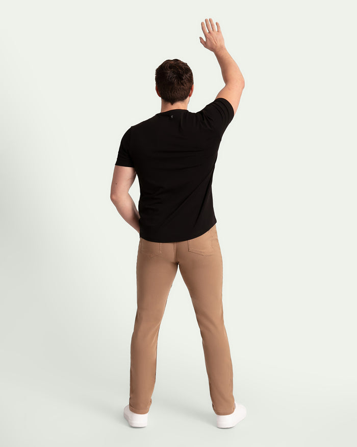 Man wearing black short-sleeve t-shirt and dark khaki slim fit pants, shown from behind.