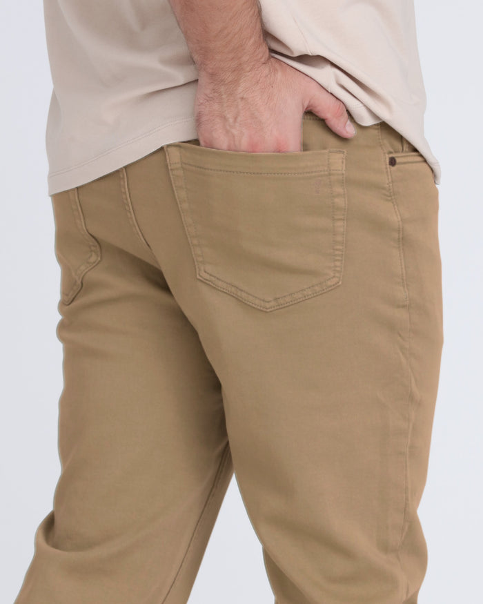 Dark khaki slim fit pants with back pocket detail, worn with cream shirt.