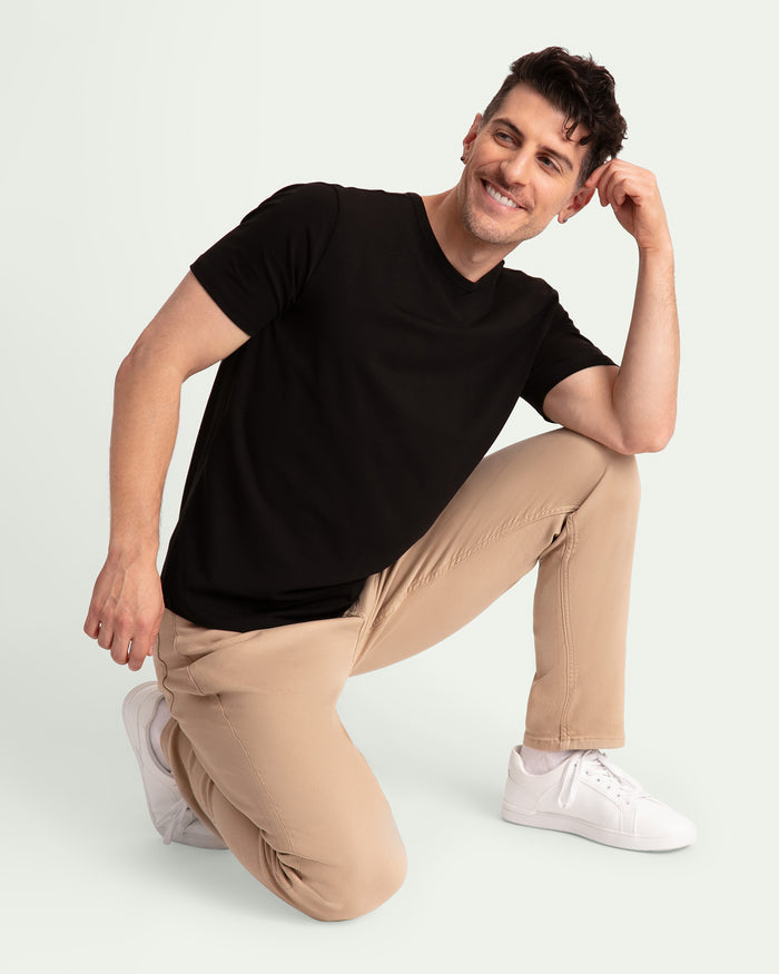 Man wearing black v-neck t-shirt and light khaki slim fit pants with white sneakers.