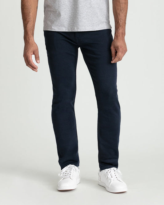 Man wearing gray t-shirt and navy slim fit jeans with white lace-up sneakers.