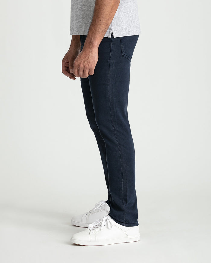 Man wearing navy slim fit jeans with white sneakers and gray t-shirt, shown from the side.