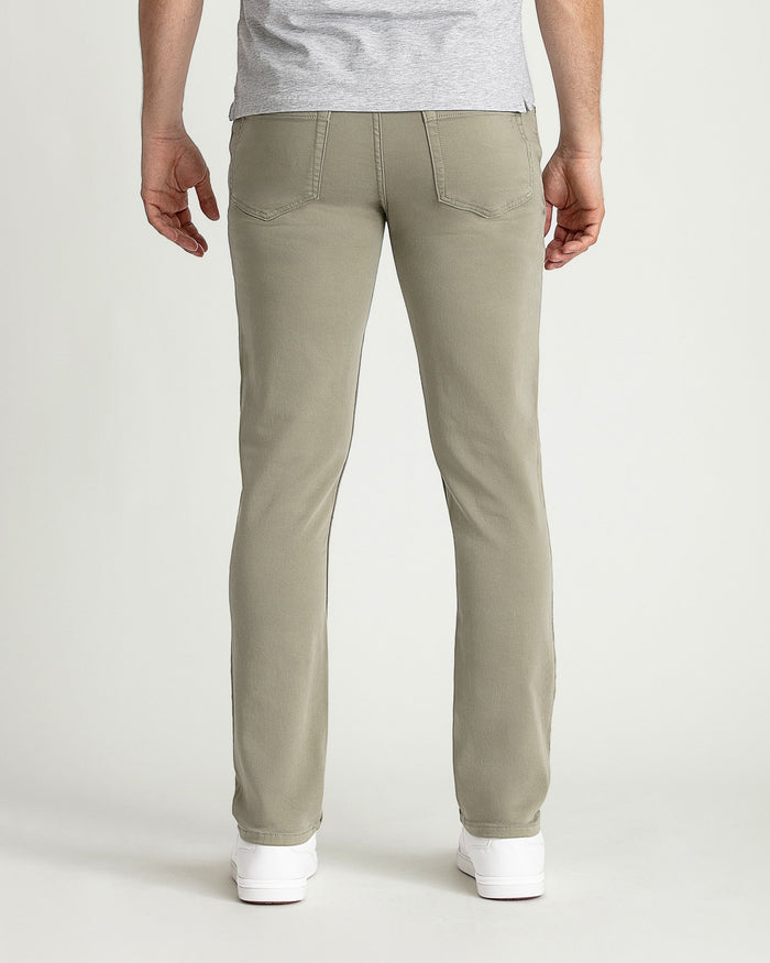 Man wearing light green slim fit pants with back pockets, shown from behind with gray t-shirt and white sneakers.