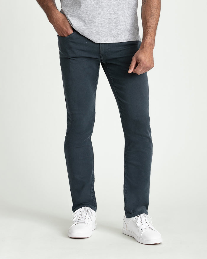 Man wearing gray t-shirt and dark slate slim fit jeans with white sneakers.