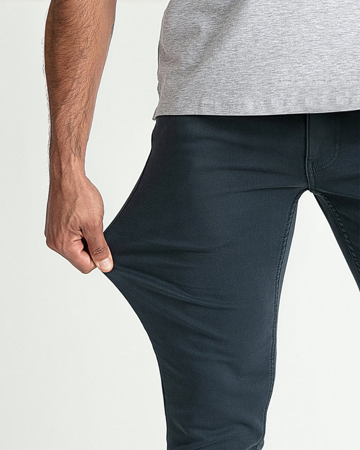 Man wearing gray t-shirt and dark slate slim fit pants, showing fabric stretch at thigh.