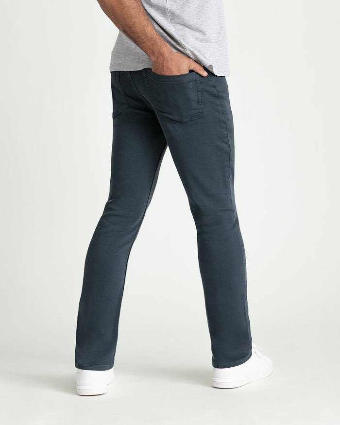 Slim fit dark slate jeans with five-pocket styling on a man wearing a gray t-shirt and white sneakers.