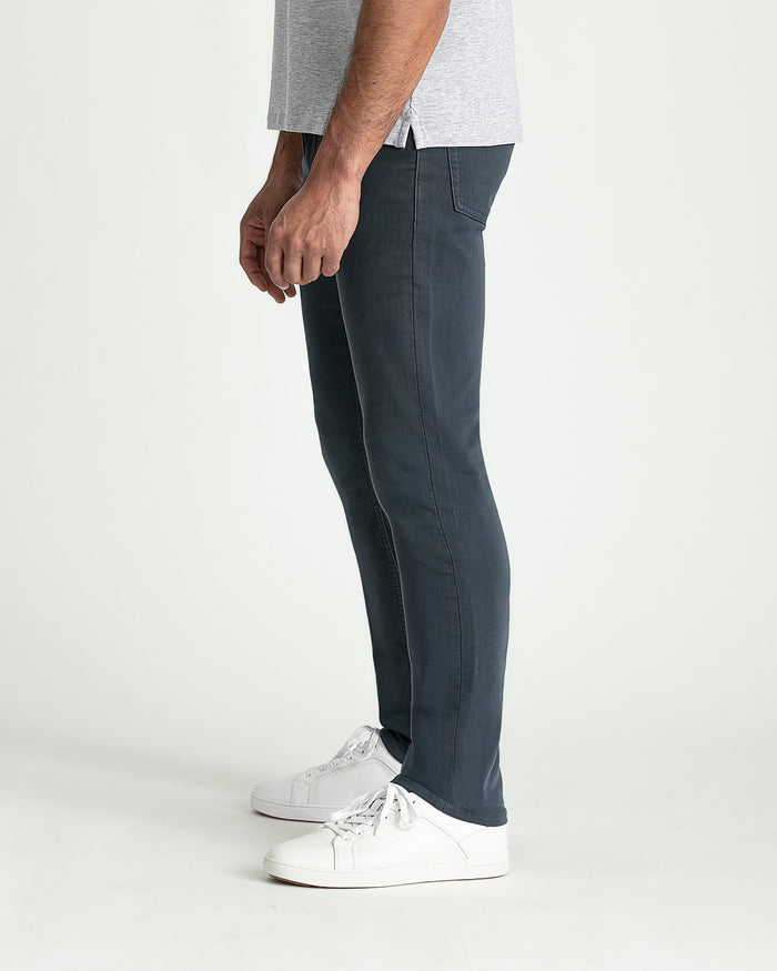 Man wearing slate-colored slim fit pants with white sneakers and light gray shirt.