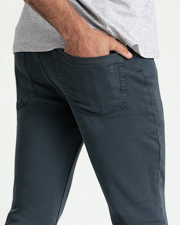 Men's slate-colored slim fit jeans with back pocket detail, worn with gray t-shirt.