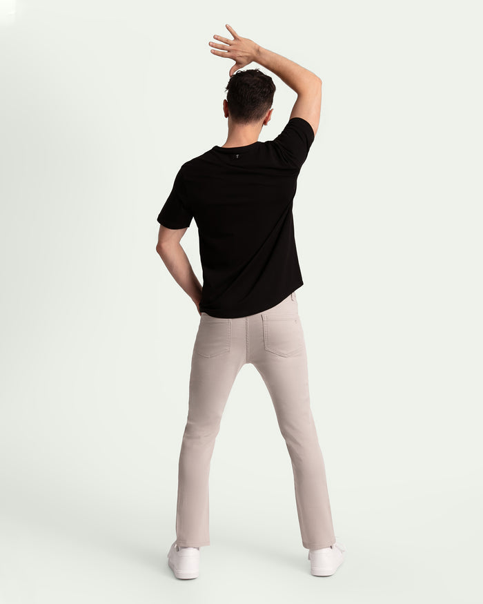 Man wearing black t-shirt and light grey slim fit pants, shown from behind.