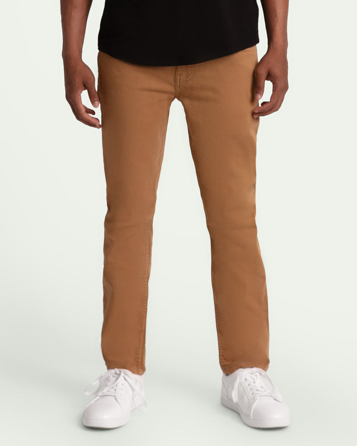 Men's slim fit brown chinos worn with black shirt and white sneakers.
