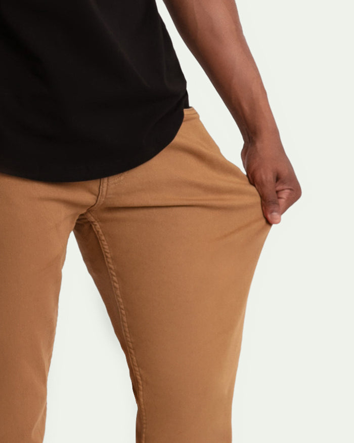 Brown slim fit pants on model wearing black shirt, showing fit through hip and thigh area.
