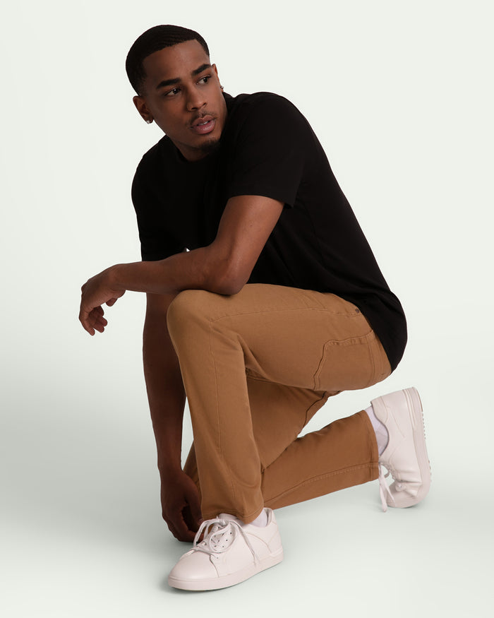 Man wearing brown slim fit pants with black t-shirt and white sneakers.
