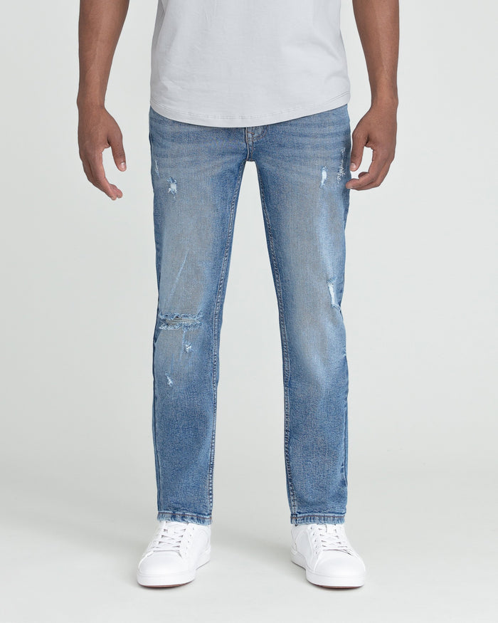 Man wearing medium blue slim fit jeans with ripped details and white sneakers.