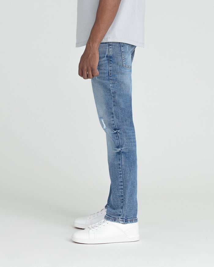 Medium blue slim fit jeans with ripped details on the thigh, worn with white sneakers.