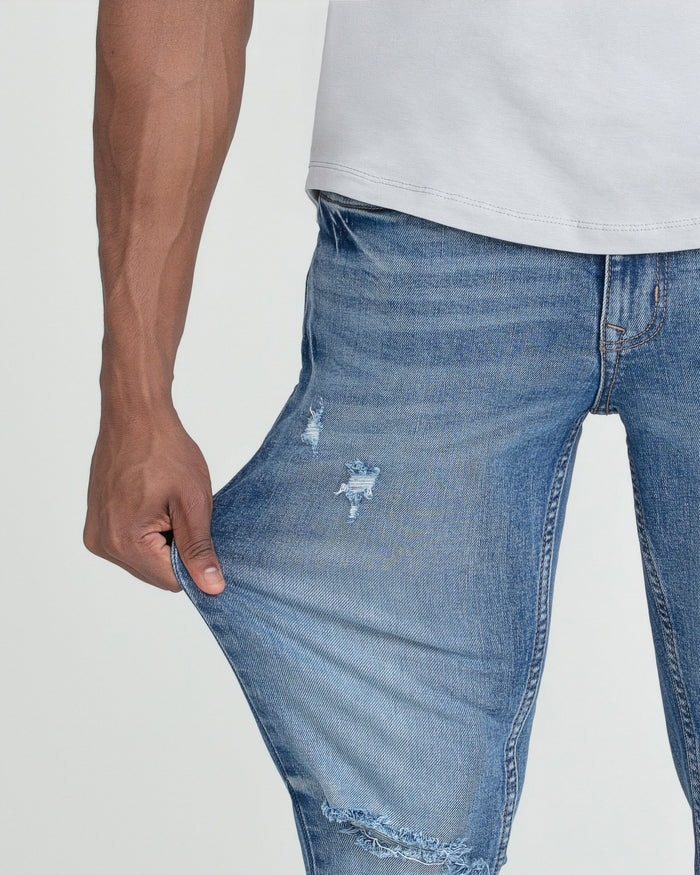 Medium blue slim fit jeans with ripped details on thigh and knee, worn with white shirt.