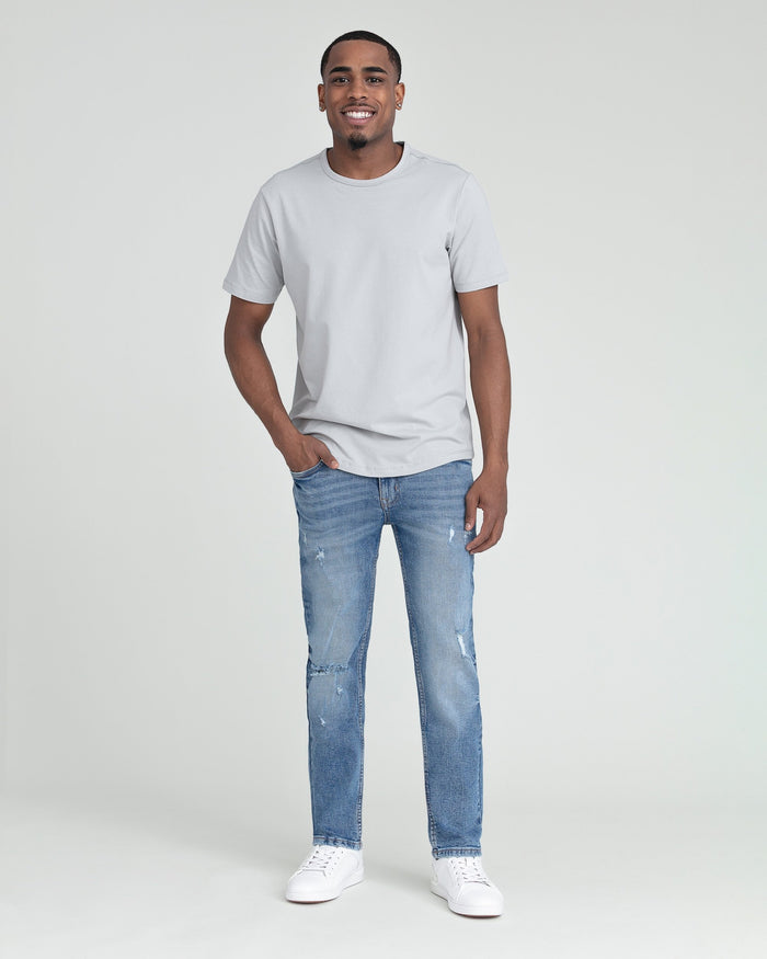 Man wearing light gray t-shirt and medium blue slim fit jeans with ripped details at thighs.