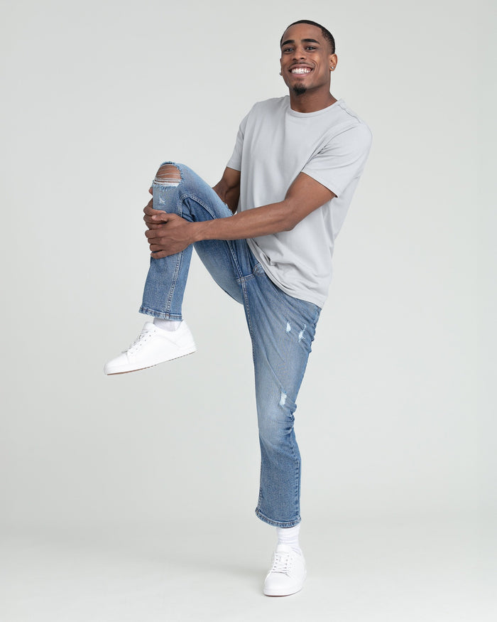 Man wearing medium blue slim fit ripped jeans with white sneakers and white t-shirt.