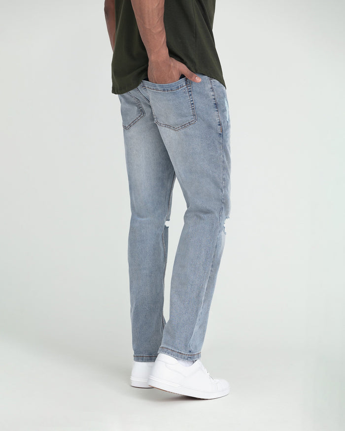 Light wash slim fit jeans with ripped details on the thighs, shown on model wearing white sneakers.