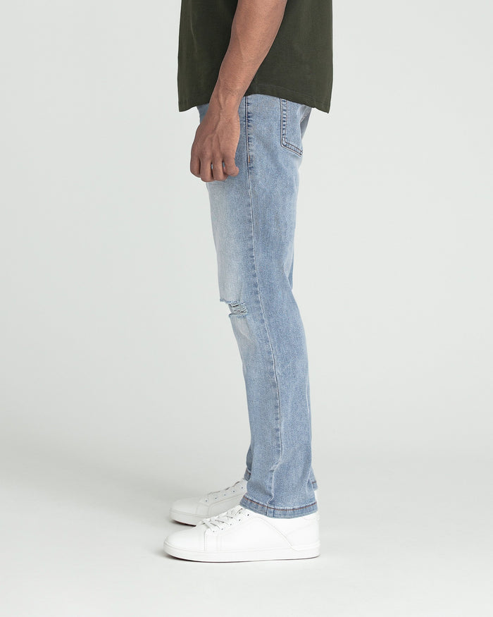 Light blue slim fit jeans with ripped knee detail, paired with olive green shirt and white sneakers.