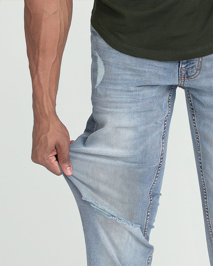 Light wash slim fit jeans with ripped details on thigh and knee, worn with olive green t-shirt.