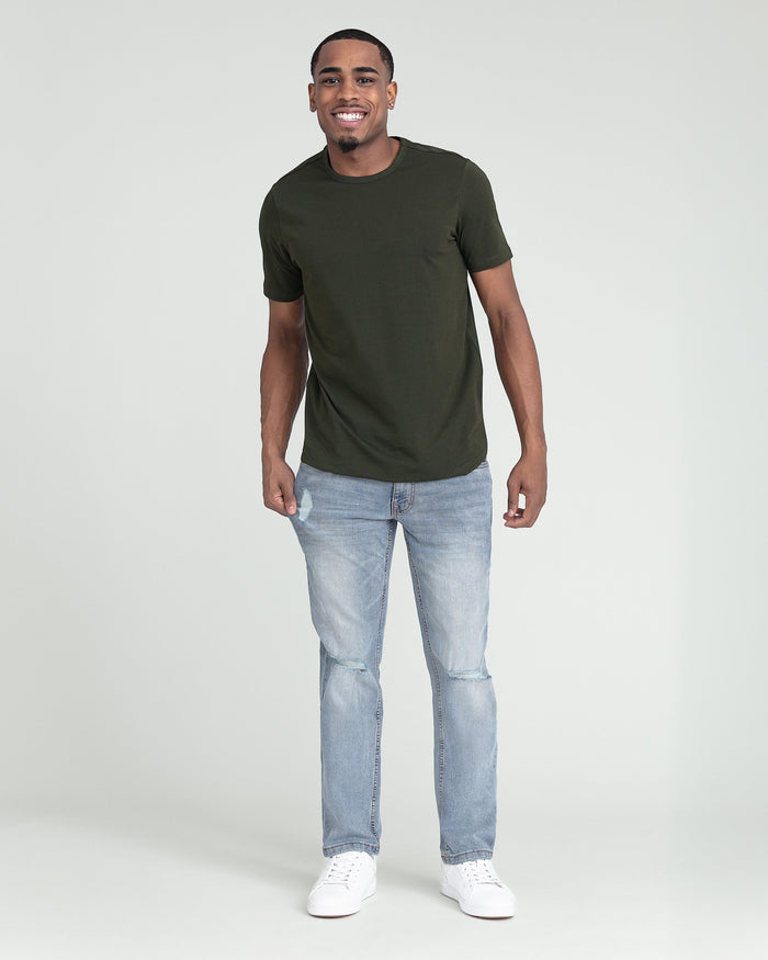 Man wearing olive green t-shirt and light wash slim fit jeans with ripped knees.