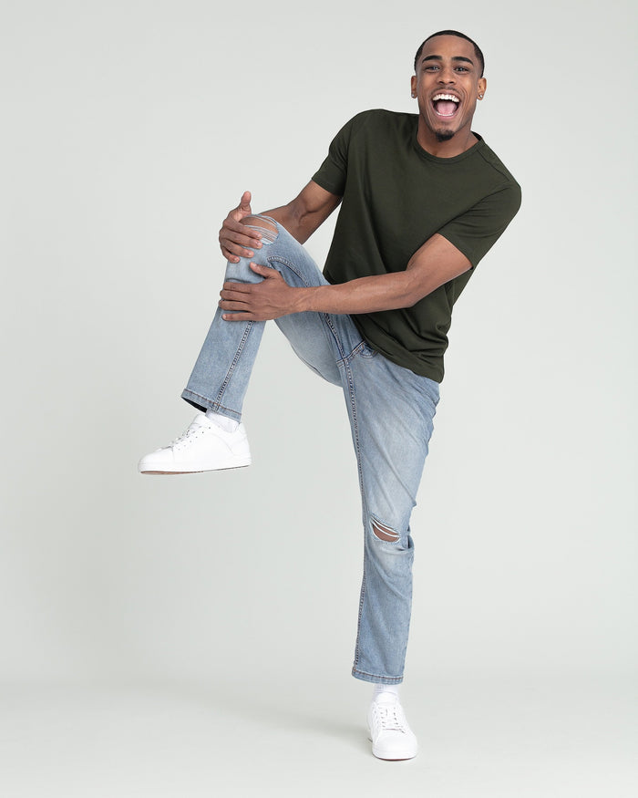 Man wearing olive green t-shirt and light-wash slim fit jeans with ripped knee detail.