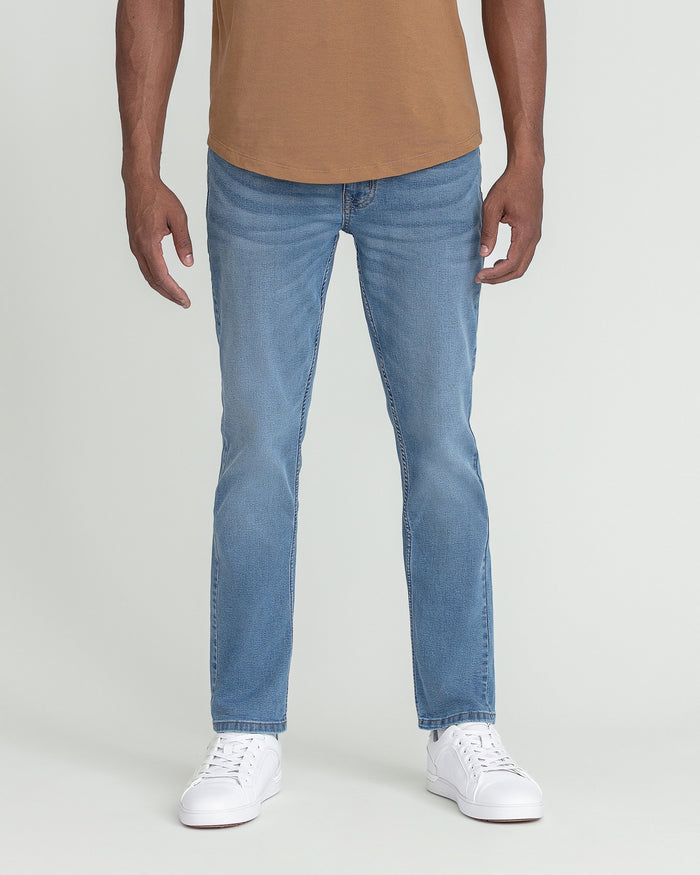 Man wearing light indigo slim fit jeans with tan shirt and white sneakers.