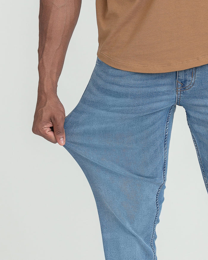 Man wearing tan t-shirt and light indigo slim fit jeans.