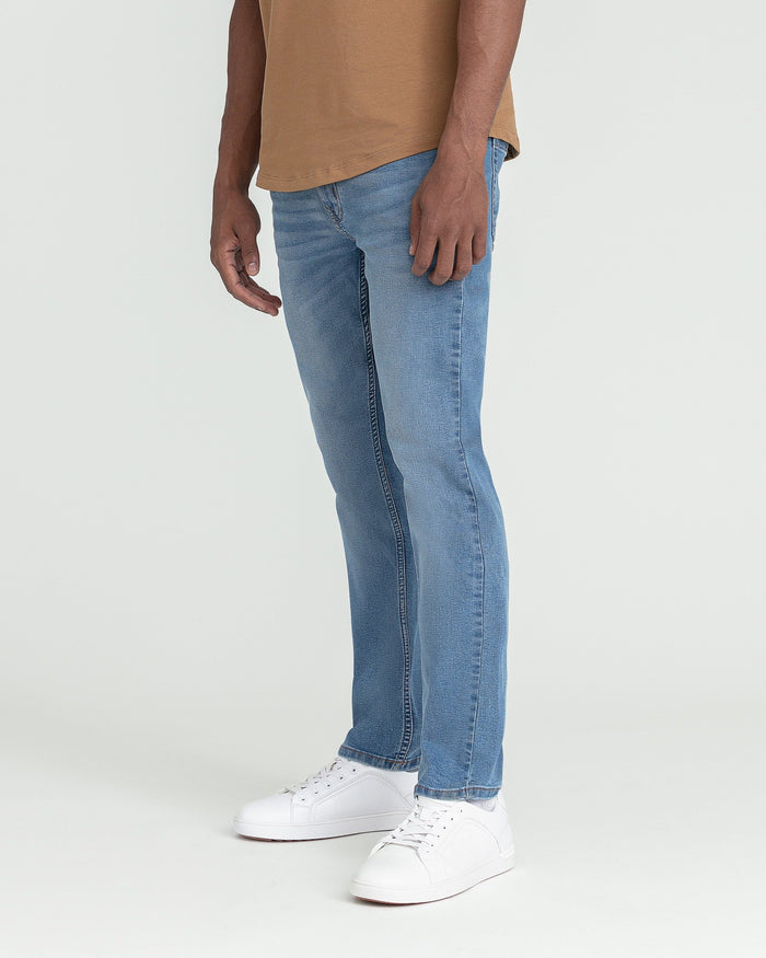 Man wearing light blue slim fit jeans with white sneakers and tan t-shirt.
